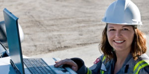 Woman wearing a hardhat working on a laptop at a construction site