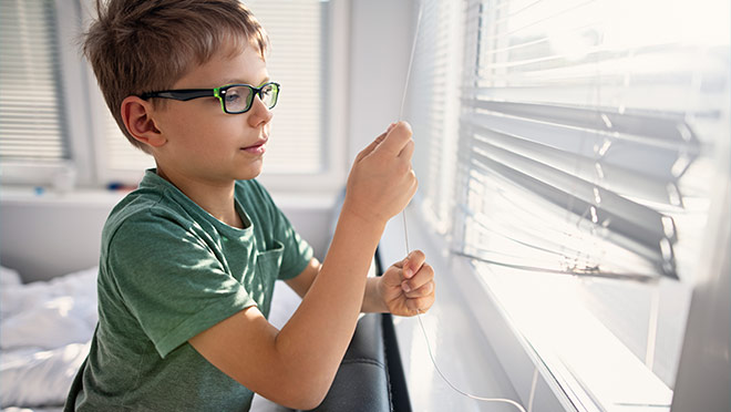 Image of a young boy closing window blinds on a bright day