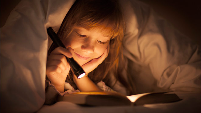 Image of a young girl using a flashlight to read a book