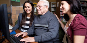 Older man learning to use a computer with two young helpers
