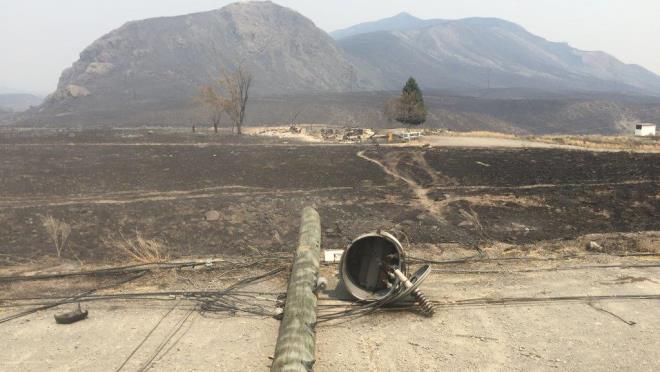 Photo from July 2017 wildfire shows a burned power pole and a charred landscape with smoky haze in the background