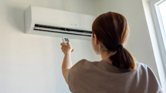 Woman adjusting heat pump with remote