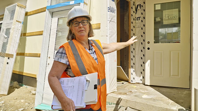 BOABC inspector in a high visibility vest and a hard hat inspects the framing of a building in construction