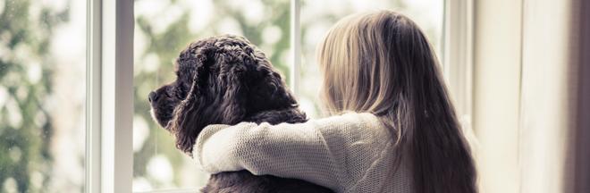 girl hugging dog looking out window