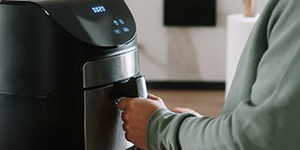 A person using an air fryer appliance in a kitchen.