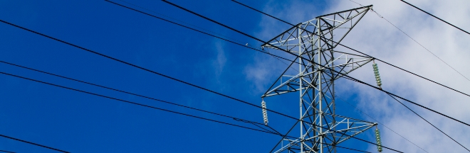 Top of transmission tower with transmission lines. In the background some blue sky and clouds