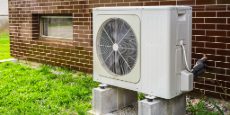 Heat pump on the wall of a brick home with part of the lawn in view.
