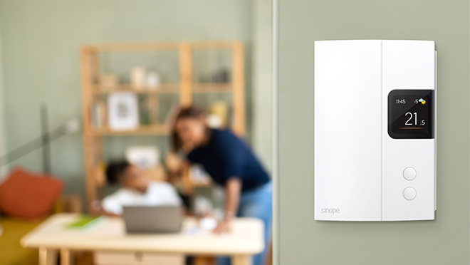 An installed smart thermostat in the foreground with family relaxing in the background.