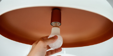 Replacing the light bulb in the luminaire, a close-up of a human hand spins a low-energy led lamp in the shade of frosted glass.