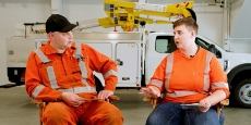 Two BC Hydro employees sitting and talking; in the backgroun a bucket truck.