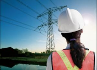 Woman in a hardhat looking on to the transmission lines crossing a farm and pond looking on to the transmission lines