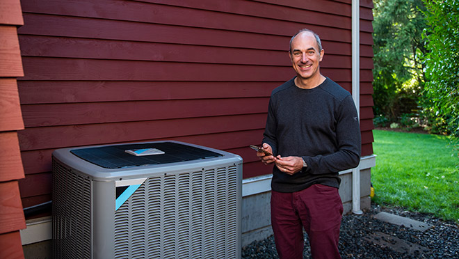 Smiling man stands beside a heat pump on a North Shore house Smiling man stands beside a heat pump on a North Shore house