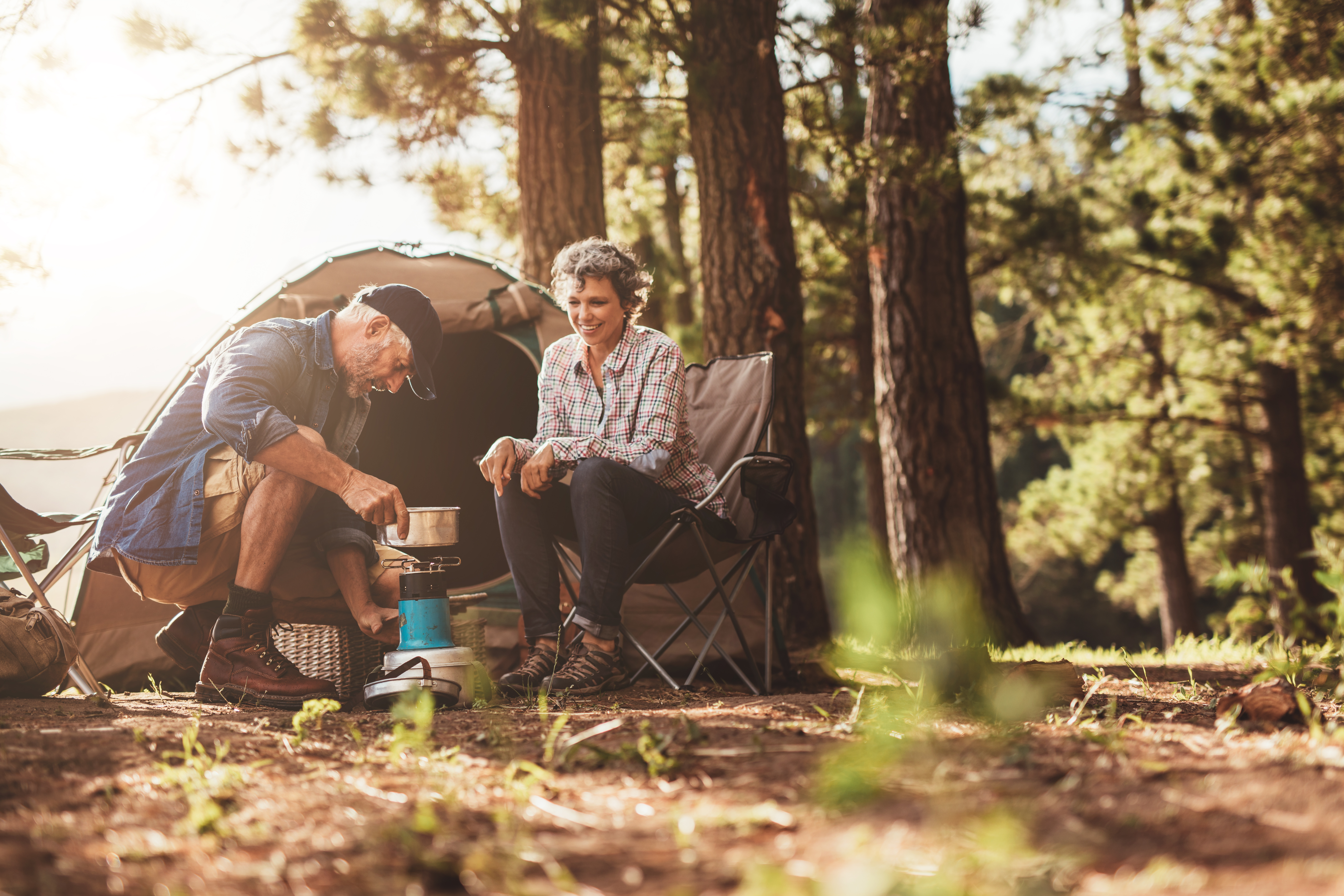 Image of senior couple camping Happy campers outdoors in the wilderness and making coffee on a stove. Senior couple on a camping holiday.