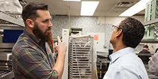 A client and a holding a clipboard contactor discussing in a commercial kitchen A client and a holding a clipboard contactor discussing in a commercial kitchen