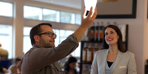 A contractor holds up a light bulb while interacting with the client behind the counter in a restaurant.