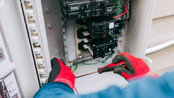 Electrician wearing safety gloves adjusting residential electrical panel with screwdriver. Electrician wearing safety gloves adjusting residential electrical panel with screwdriver.