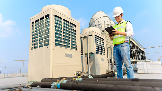 Image of an engineer standing next to rooftop HVAC units Image of an engineer standing next to rooftop HVAC units