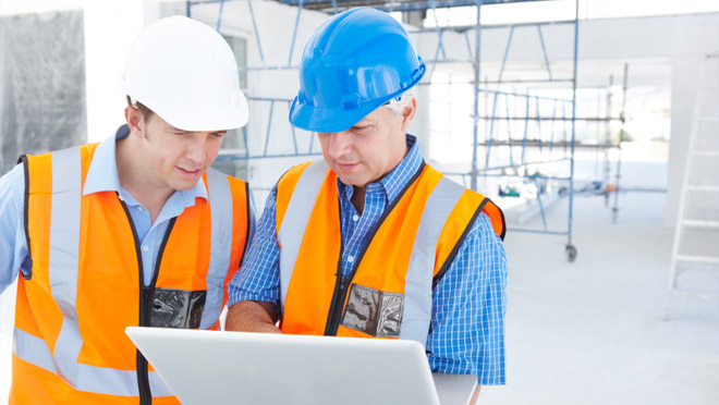 Two workers in safety gear looking at a laptop Two workers in safety gear looking at a laptop