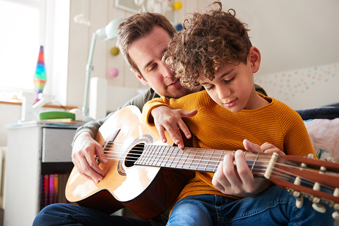 A father teaching his son how to play an acoustic guitar