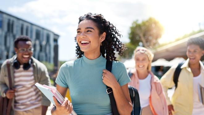A happy female student walking together with friends on a university campus on a sunny day.