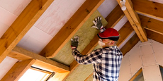 Worker installs pink fiberglass insulation in an attic