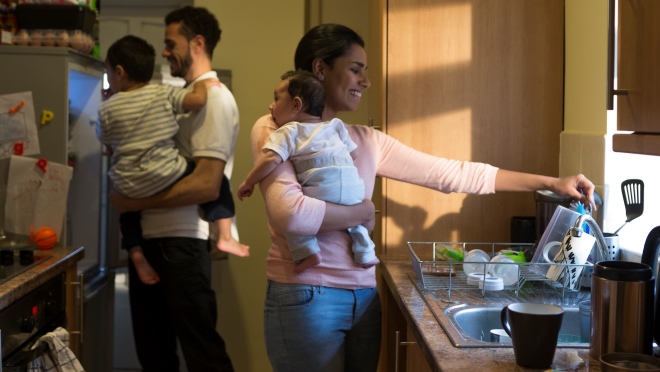 Couple holding a baby each work in kitchen A mother and father carry babies as they do chores around their kitchen.