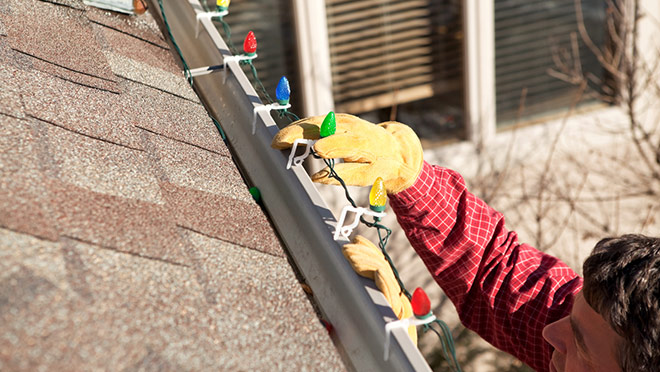 Image of man on a ladder installing lights on a house roof
