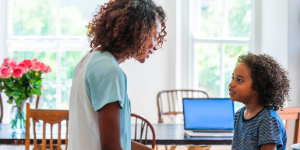 A photo of young woman communicating with girl. Side view of female looking at daughter in kitchen. They are wearing casuals at home.