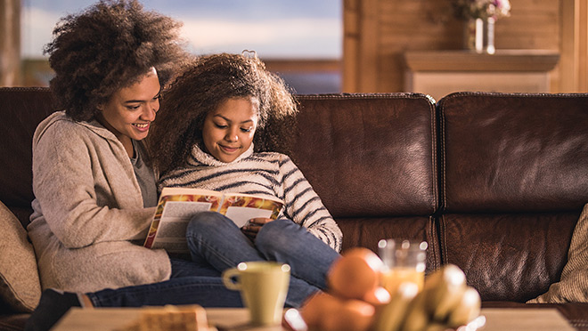 Happy mother and daughter sitting on a sofa and reading a book