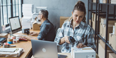 Two people working in an office setting focused on packaging and shipping tasks.