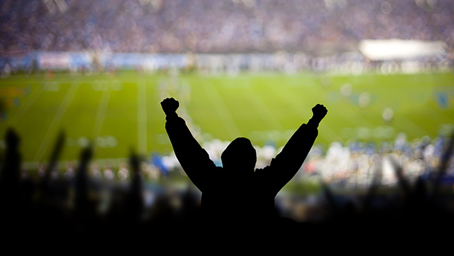 Silhouetted fans cheering in a crowded football stadium