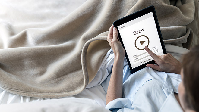 Image of person brewing coffee while using a tablet in bed Image of person brewing coffee while using a tablet in bed