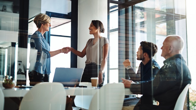 two businesswomen shaking hands together during a boardroom meeting at work
