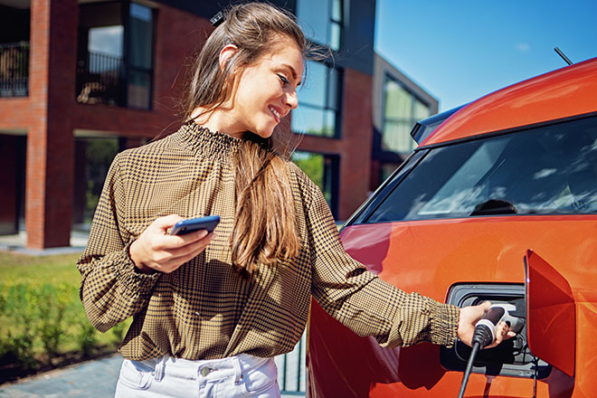 A woman connects an EV to charger on a sunny summer day