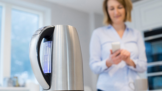 Woman controlling smart kettle using app on mobile phone Woman controlling smart kettle using app on mobile phone
