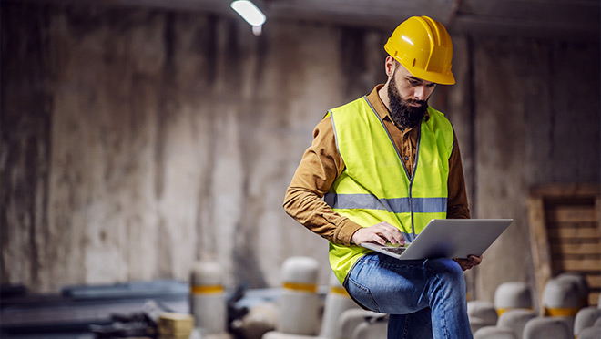 Image of a worker wearing a high-vis vest and working on a laptop