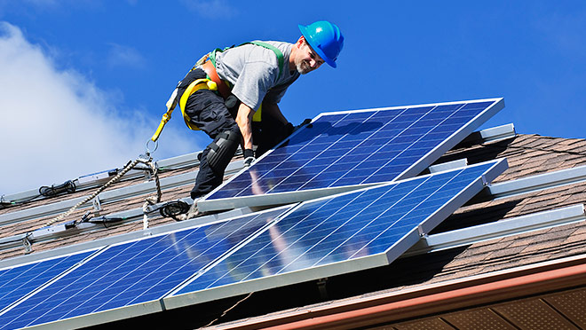 Image of worker installing solar panels on a house roof