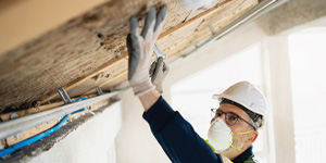 A professional worker in protective gear installing insulation in a residential building's attic.