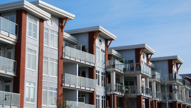 Multi-floor residential building with vertical red-brick framing grey paneling on its exterior with balconies.
