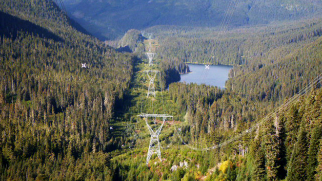 Transmission towers and lines running through a forest past a lake.
