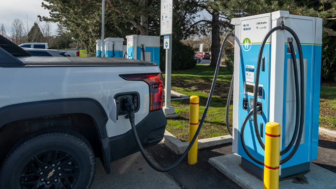 A white electric pickup truck at a public BC Hydro charging station in Delta with trees and grass in the background. A white electric pickup truck at a public BC Hydro charging station in Delta with trees and grass in the background.