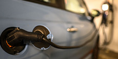 Electric car charging with close-up of plugged charging cable. Charging station blurred in background.