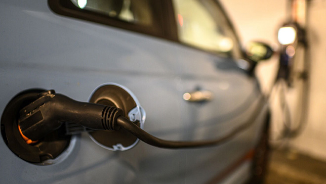 Electric car charging with close-up of plugged charging cable. Charging station blurred in background. Electric car charging with close-up of plugged charging cable. Charging station blurred in background.