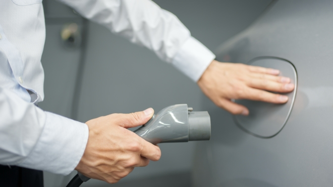 Person charging an electric vehicle. Person about to open the charging port of an electric vehicle to connect the plug.