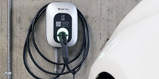 A wall-mounted SWTCH electric vehicle charging station with coiled charging cable in an indoor parking garage, next to a white EV.