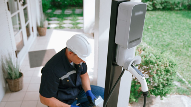 Technician in hard hat installs electric vehicle charging station on a residential porch. Technician in hard hat installs electric vehicle charging station on a residential porch.