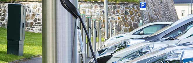 A row of electric cars plugged in to charging stations in a parking lot A row of electric cars plugged in to charging stations in a parking lot