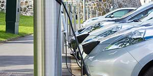 A row of electric cars plugged in to charging stations in a parking lot