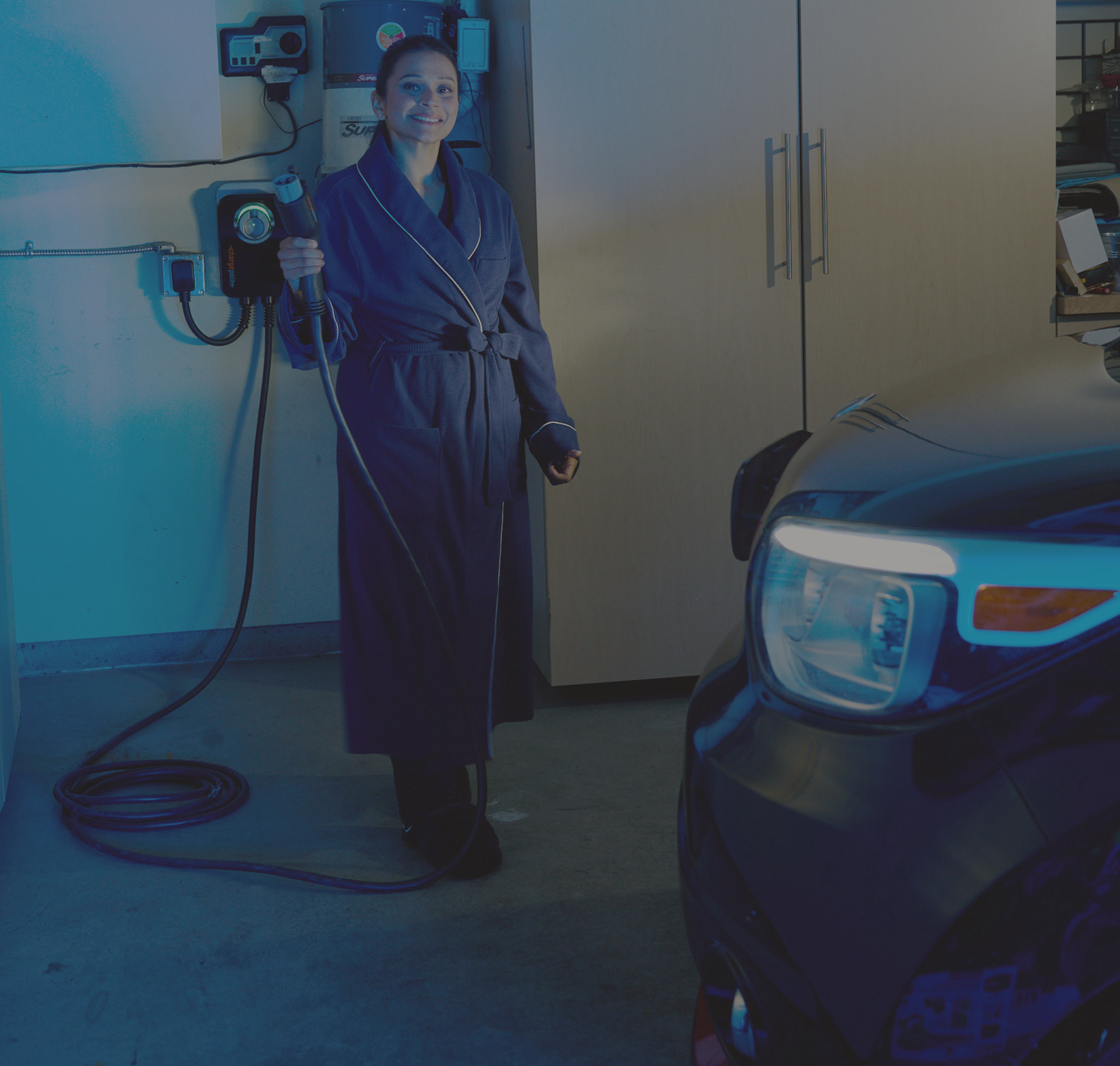Person standing in a car garage at home holding a car charger plug with car in the right side of the image