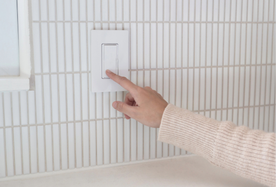 In this image, a persons hand is touching a light dimmer on a wall.